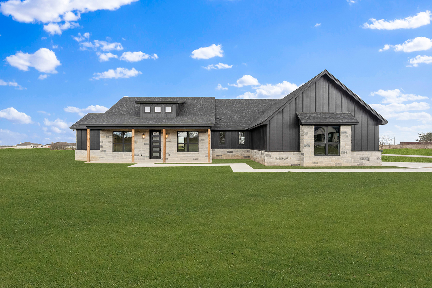 Black board-and-batten custom home with limestone accents and cedar porch posts