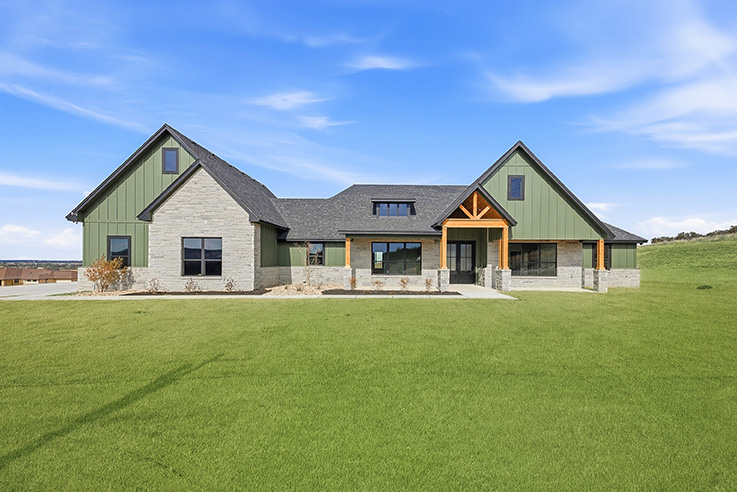 Sage green board-and-batten and limestone custom home on an open lawn