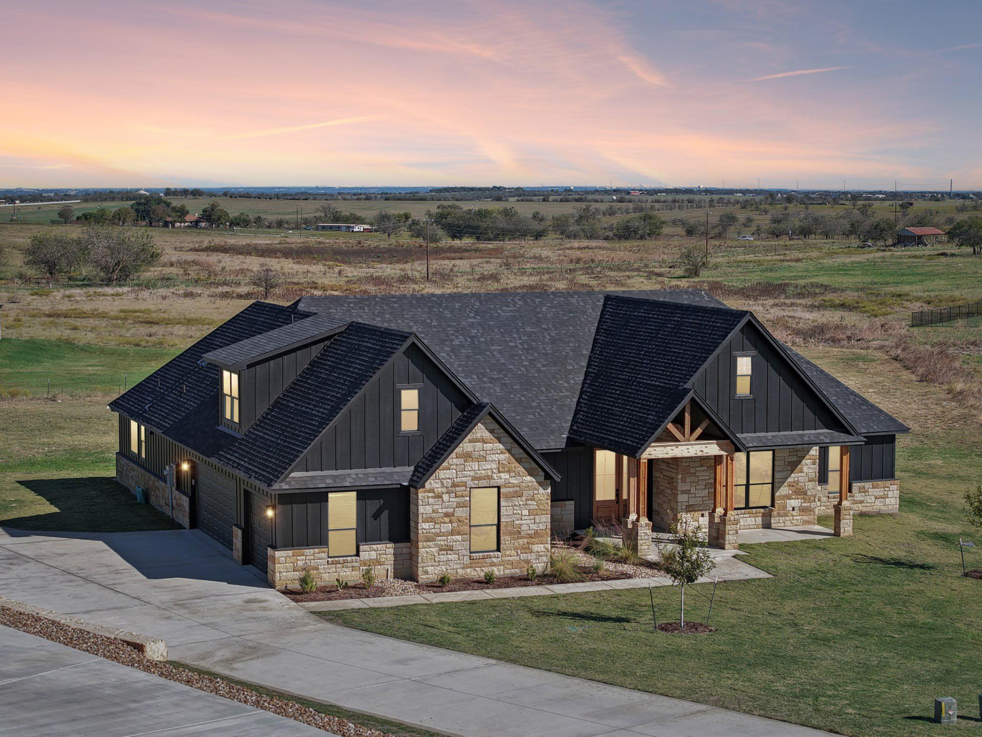 Newly built black board-and-batten and stone custom home on acreage at sunset