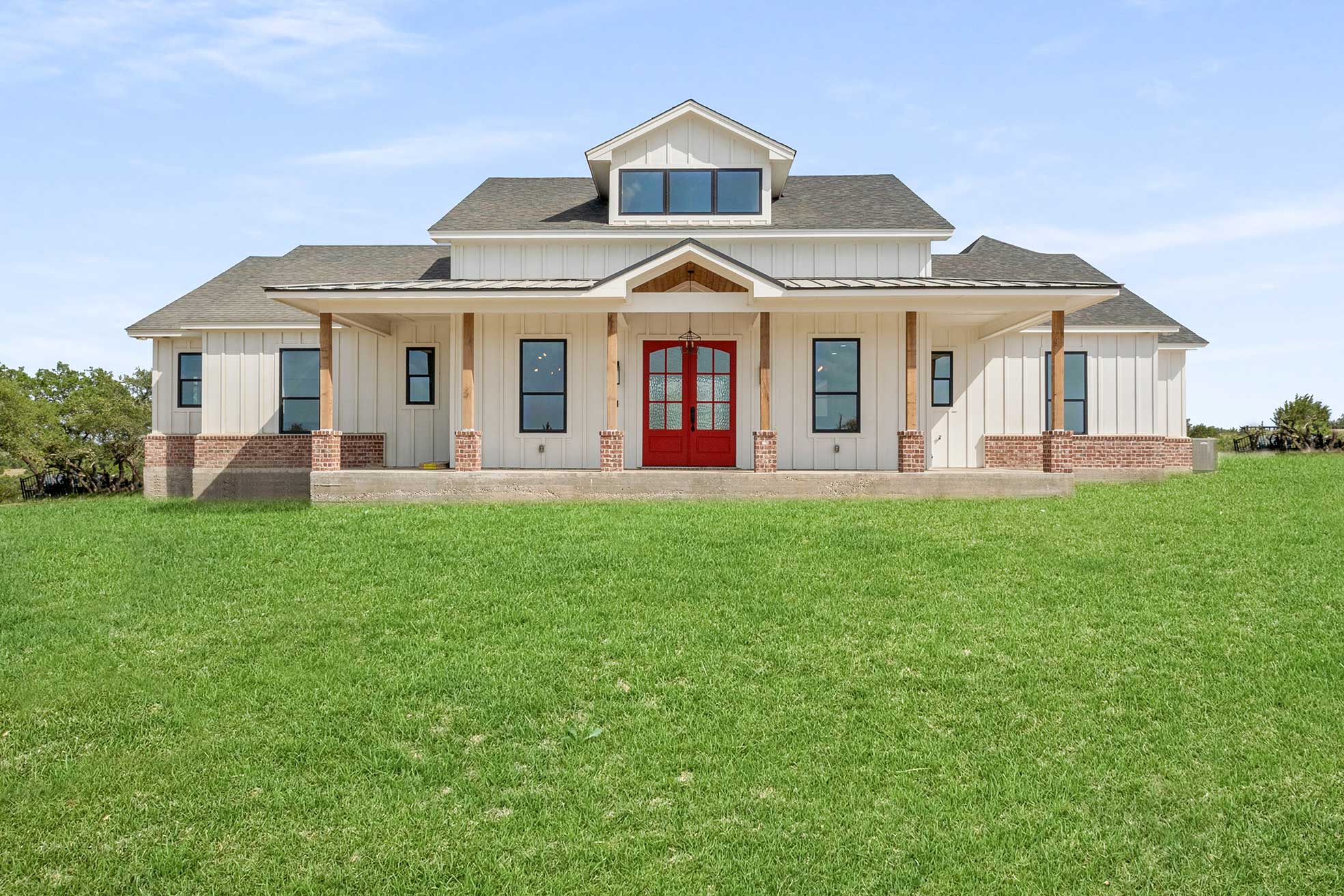 White board-and-batten ranch home with brick skirt and red front door