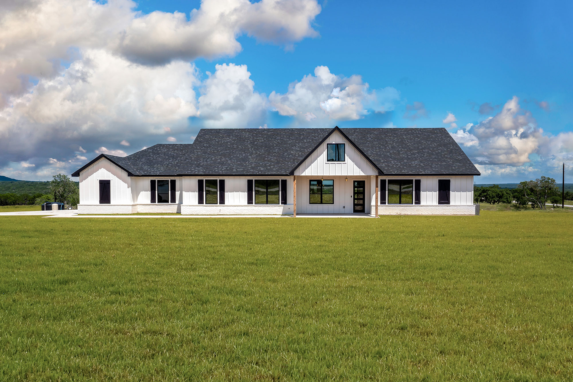 Long white modern farmhouse with black shutters on hill country acreage